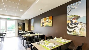 A dining area with tables set for service, artwork on the walls, and a view through the windows. - Brit Hotel Binic (Binic-Etables-sur-Mer)