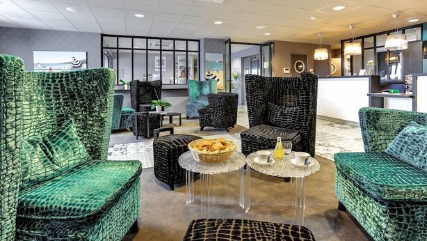 A lobby with green patterned sofas, a reception desk, and a coffee table with a basket and cups. - Brit Hotel Binic (Binic-Etables-sur-Mer)