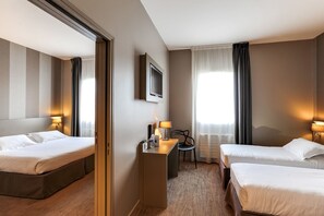 A hotel room with two beds, a desk, a chair, a TV, and a window with curtains. - Brit Hotel Binic (Binic-Etables-sur-Mer)