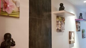 A modern interior with a red shelf holding a statue, a large flower decoration, and a dark tiled wall. - Relais Du Silence Le Clos De Pradines (Saint-Quentin-la-Poterie)