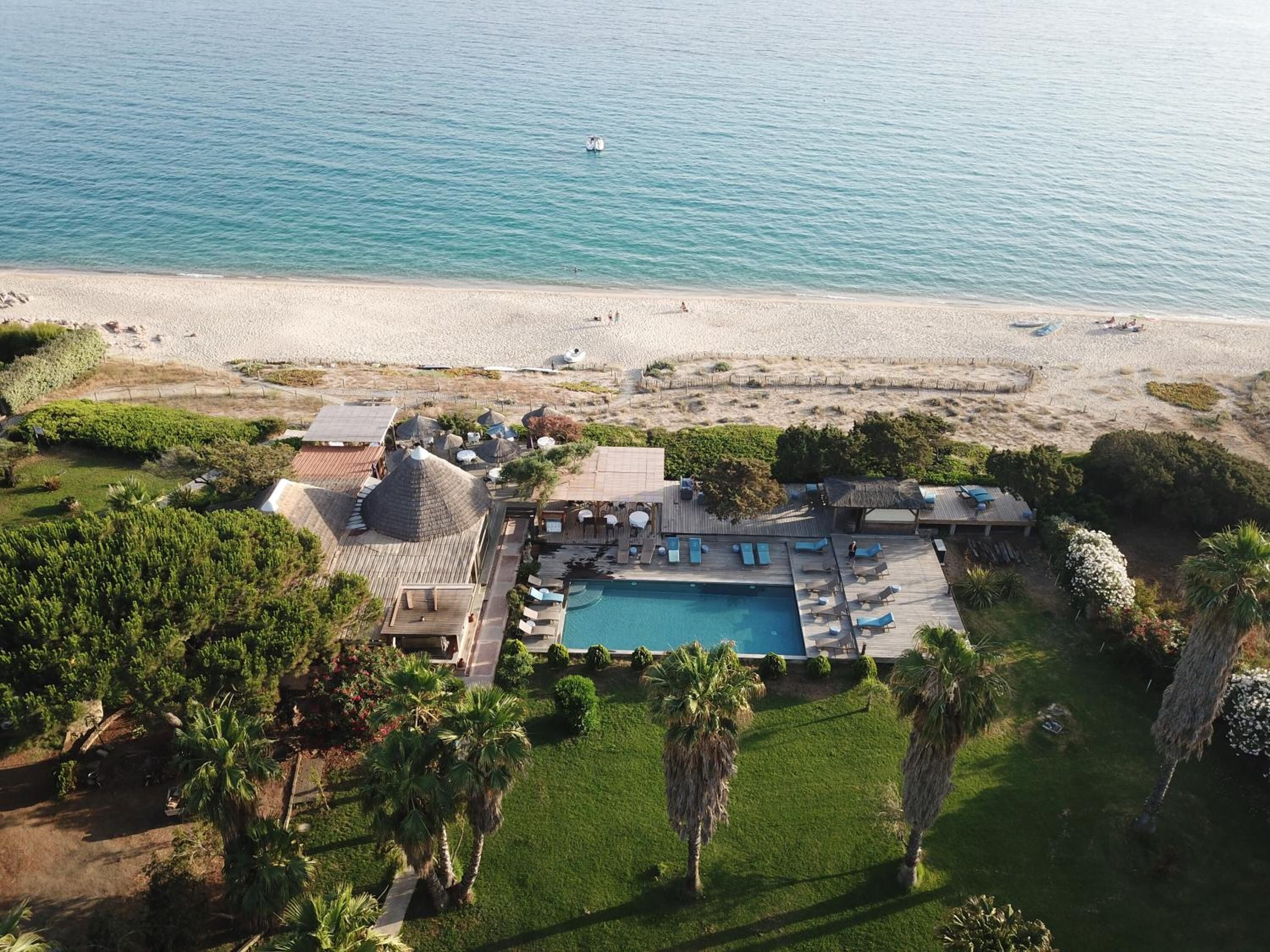Vista aérea de un resort con piscina, acceso a la playa y palmeras.