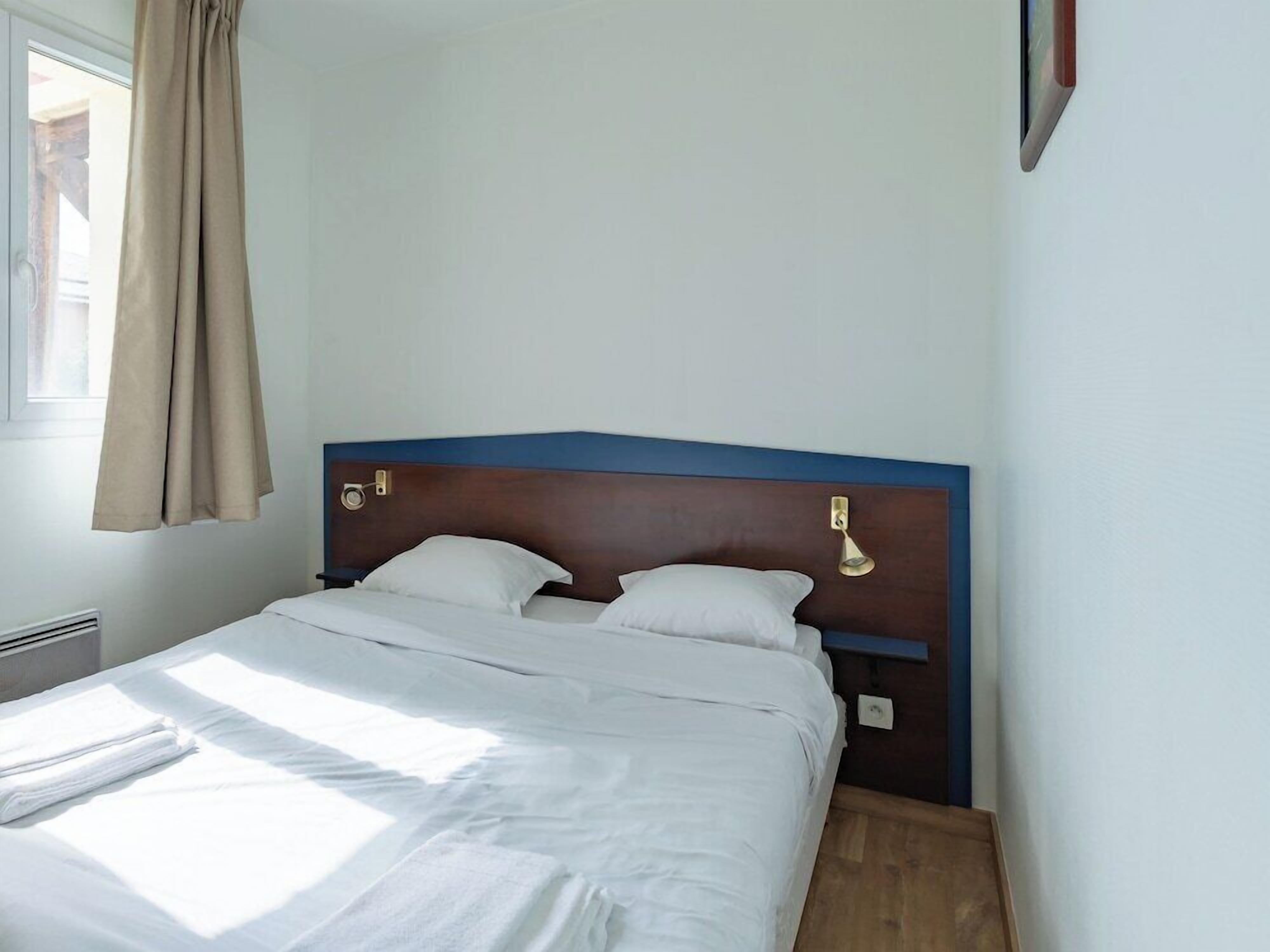 A neatly made bed with white linens, a wooden headboard, and a bedside lamp.