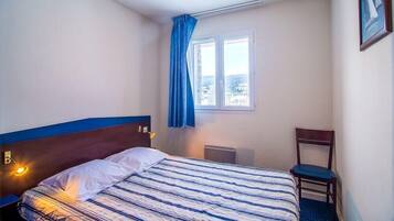 Une chambre d’hôtel avec un lit, une chaise, une fenêtre avec des rideaux et un radiateur.