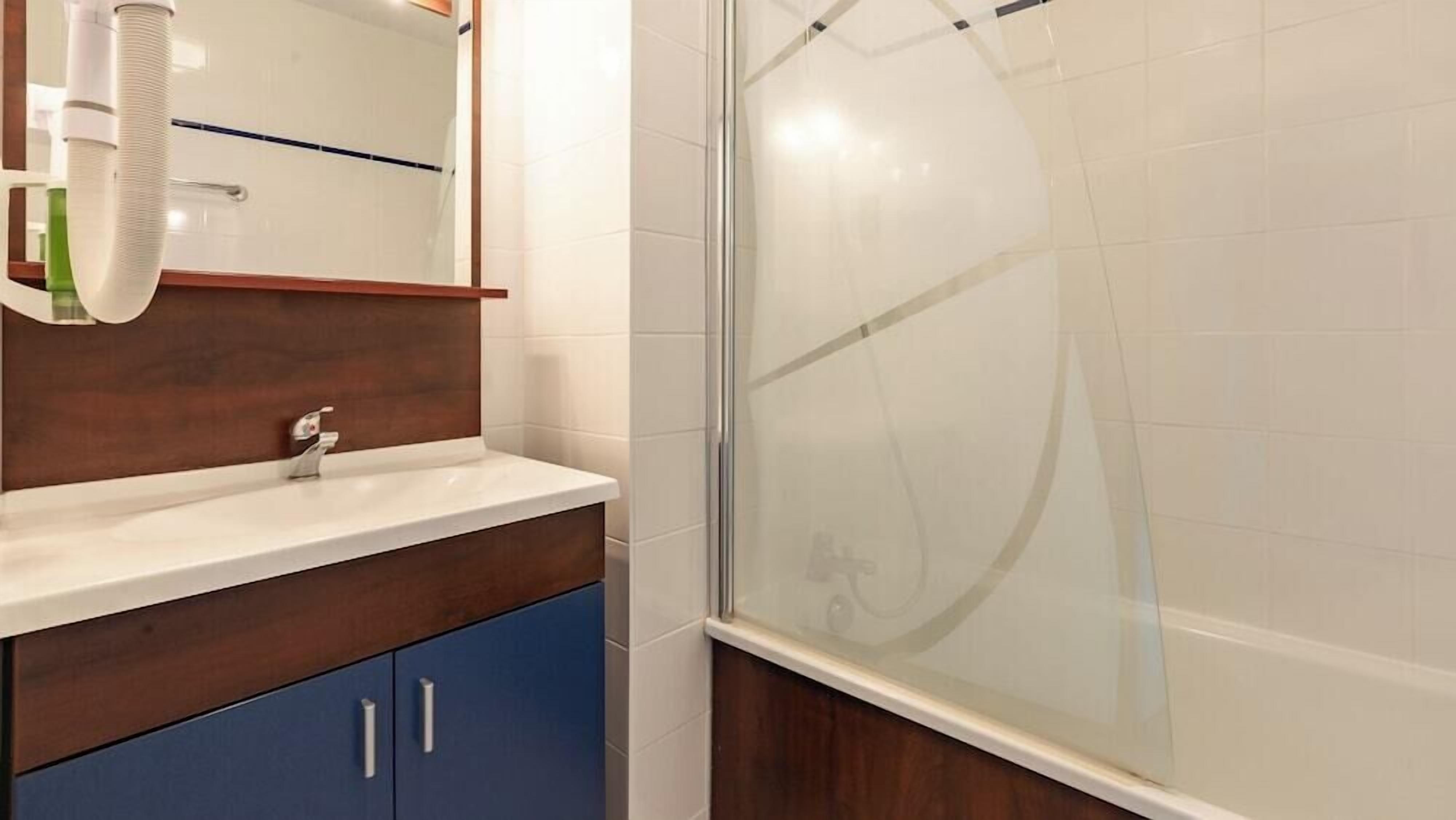 Un baño con lavamanos blanco, tocador de madera y cabina de ducha con mampara de vidrio.