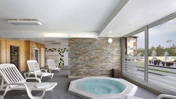 A modern indoor pool area with lounge chairs, a hot tub, and a stone wall. - Residence Appart Vacances Pyrenees 2000 (Bolquere)