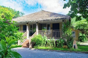 Ein Bungalow mit einem Reetdach und einer Holzterrasse, umgeben von üppiger Vegetation.