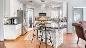 A modern kitchen with white cabinetry, a central island with bar stools, a stainless steel refrigerator, and a microwave. - 2 Suites, 6 Beds +Sofa Bed | Sauna|Sleeps 14 (Calgary)