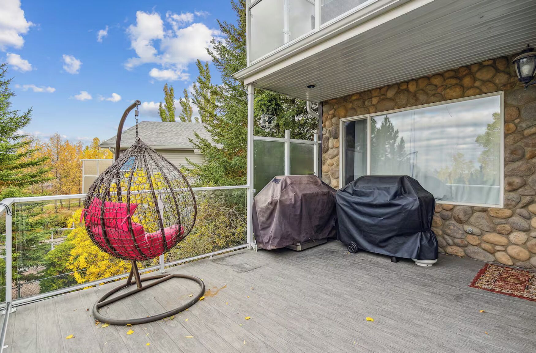 A covered outdoor area with a hanging chair, covered grill, and a stone wall.