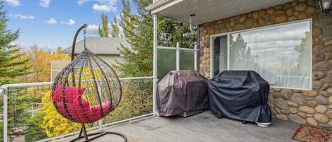 A covered outdoor area with a hanging chair, covered grill, and a stone wall.