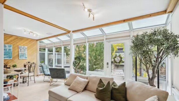 A modern living room with a sofa, a dining area, and a large window providing a view of the outdoors. - 2 Suites, 6 Beds +Sofa Bed | Sauna|Sleeps 14 (Calgary)