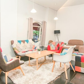 A modern living room with a sofa, chairs, a small table, and a TV. - Kapal Garden Hotel (Malang)