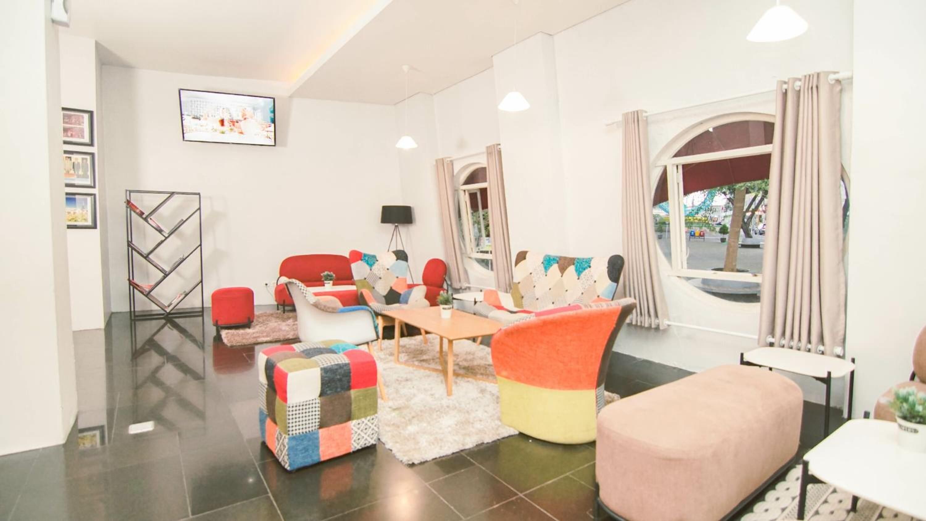 A modern living room with a sofa, ottoman, and coffee table, a TV mounted on the wall, and a window with curtains.