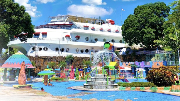 A large cruise ship docked at a port with a colorful water park in the foreground.