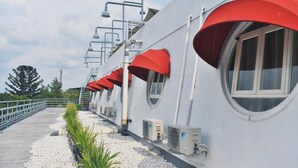 A row of windows with red awnings, air conditioning units, and a metal railing along a pathway.