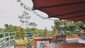 An outdoor seating area with tables and chairs, surrounded by greenery and a metal railing.