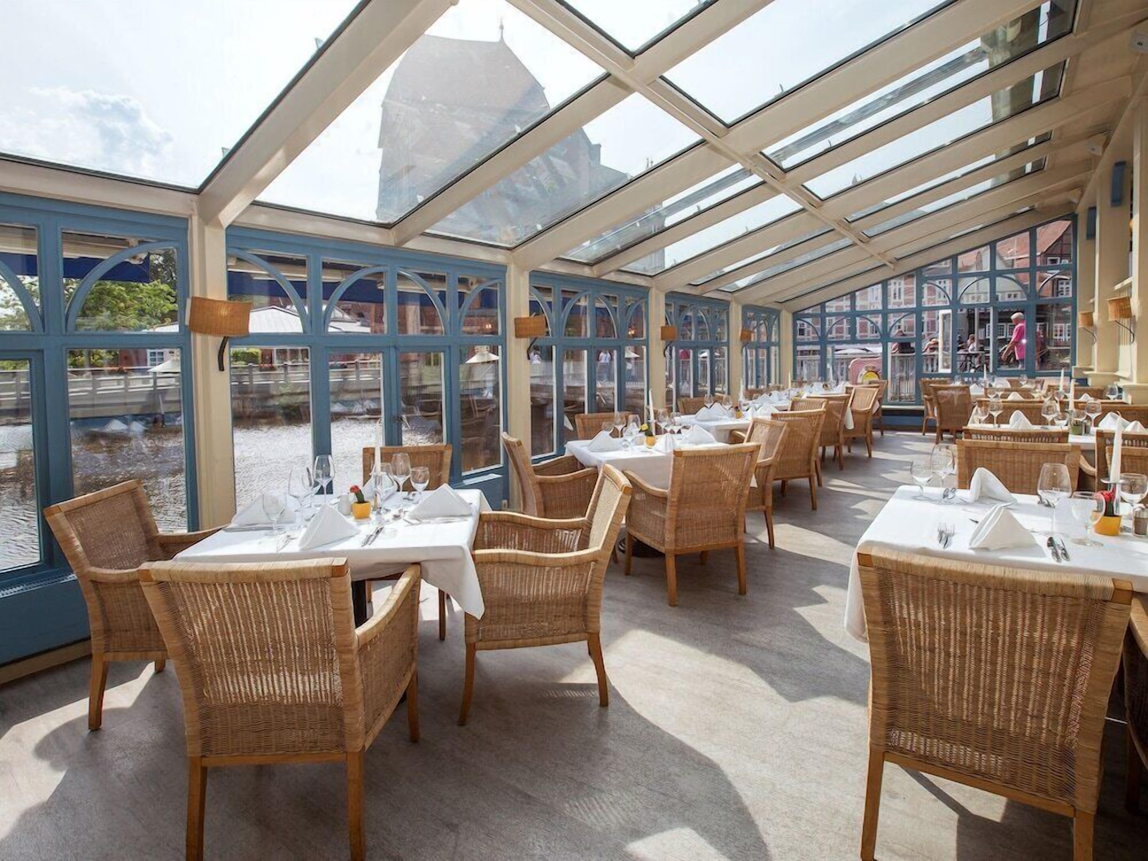 Ein Restaurant mit Glasdach, Korbmöbeln und gedeckten Tischen.