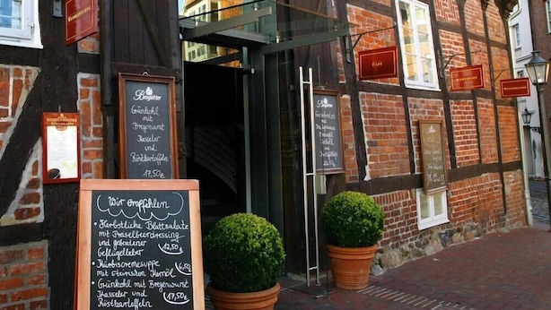 Ein traditionelles europäisches Gebäude mit Backsteinfassade, Glastür und mehreren Schildern, die auf ein Restaurant oder Café hinweisen.