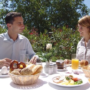 A dining table with a variety of food items and drinks, set outdoors with greenery in the background. - Seligweiler (Elchingen)