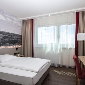 A hotel room with a bed, a desk, a chair, a lamp, and a large window with curtains. - Seligweiler (Elchingen)