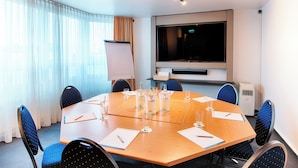 Un salón de conferencias con una gran mesa, sillas, una pantalla de proyector y un televisor.