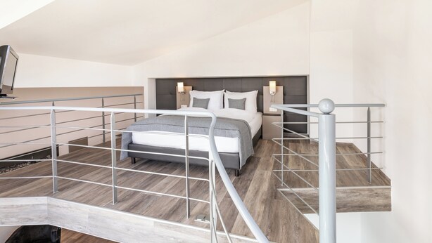Un dormitorio moderno con una cama, mesitas de noche y una escalera con barandilla.
