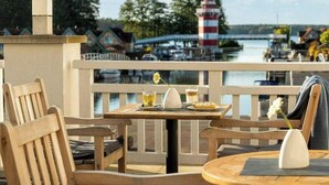 A wooden deck with a table and chairs, overlooking a body of water with a lighthouse and buildings in the background. - Precise Resort Hafendorf Rheinsberg (Rheinsberg)