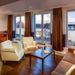 Ein modernes Wohnzimmer mit einer Couch, Sesseln, einem Couchtisch und Blick auf eine verschneite Landschaft durch große Fenster.