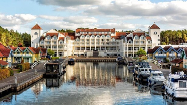 A large hotel with multiple stories, a central courtyard, and boats docked in a canal. - Precise Resort Hafendorf Rheinsberg (Rheinsberg)