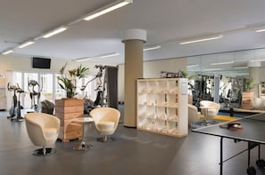 Ein modernes Fitnessstudio mit Trainingsgeräten, Sitzbereichen und einer Spiegelwand.