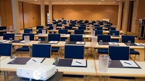 Una sala conferenze con file di tavoli, sedie e un proiettore.