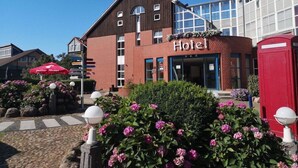 Un hotel con un cartello ben visibile che riporta la scritta 'Hotel', una cabina telefonica rossa e un ombrello rosso.