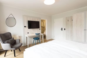Ein Schlafzimmer mit einem großen Bett, einem Schreibtisch mit Stuhl, einem Fernseher und einem Kleiderschrank.