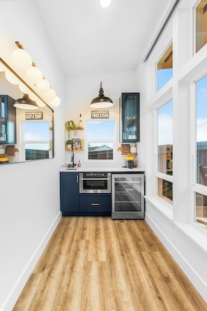 A modern kitchen with a built-in oven, a microwave, and a refrigerator. There are two windows providing natural light and a view of the outside.