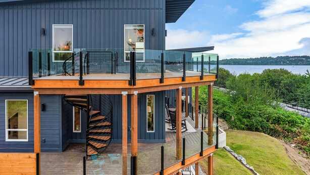 Una casa moderna de varios pisos con un balcón de vidrio, una escalera en espiral y vistas a un cuerpo de agua.
