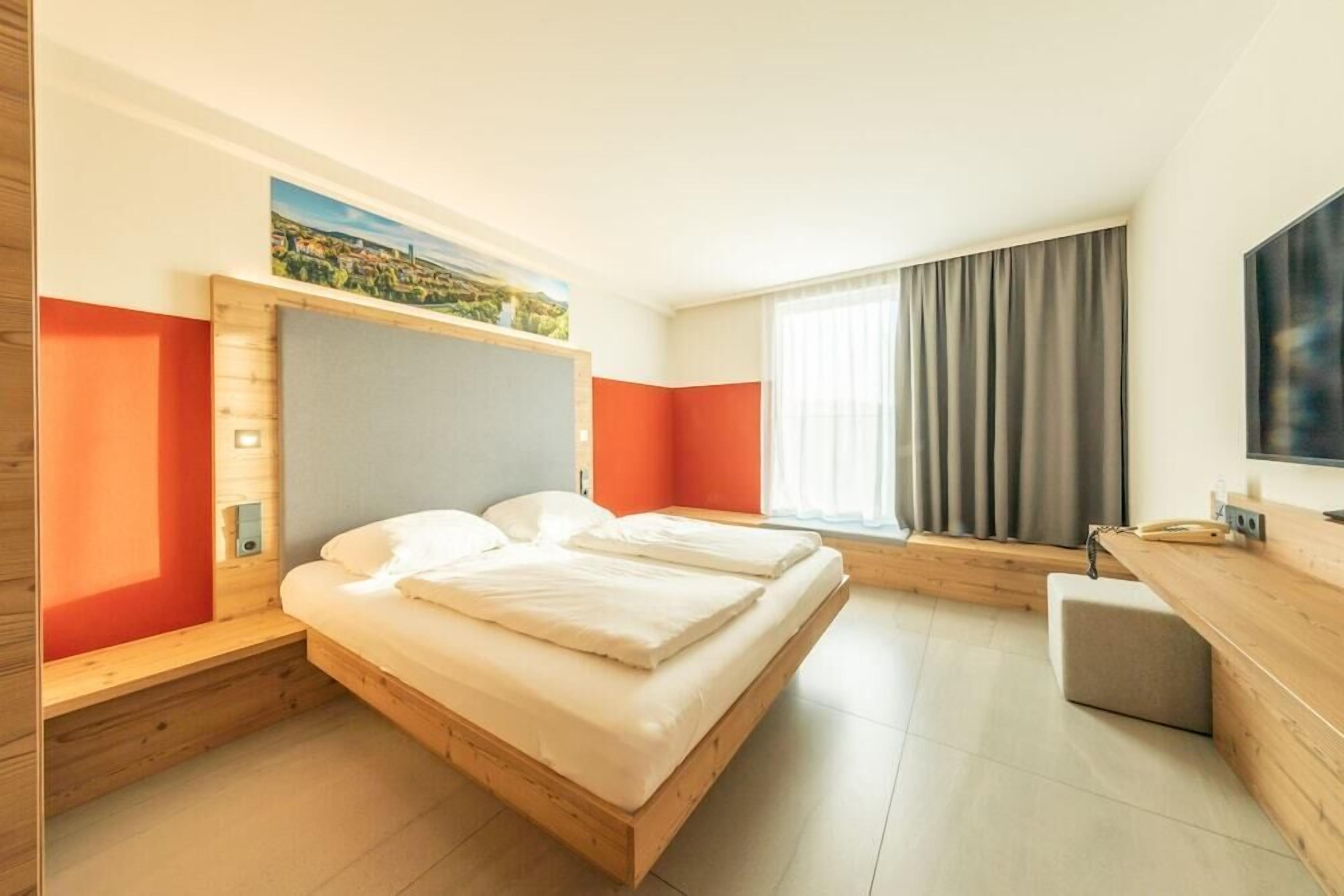 Ett modernt hotellrum med en stor säng, ett skrivbord och ett fönster med gardiner.