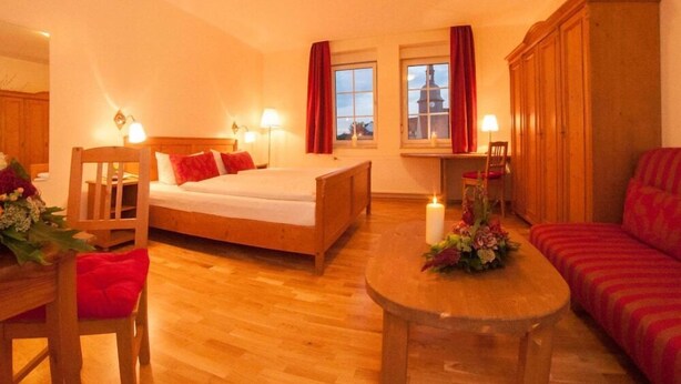 A cozy hotel room with a wooden bed, a small desk, a sofa, and a dining table with flowers. - Eisenacher Hof (Eisenach)