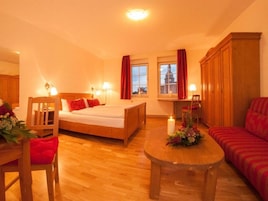 Una habitación de hotel acogedora con una cama de madera, un escritorio pequeño, un sofá y una mesa de comedor con flores.