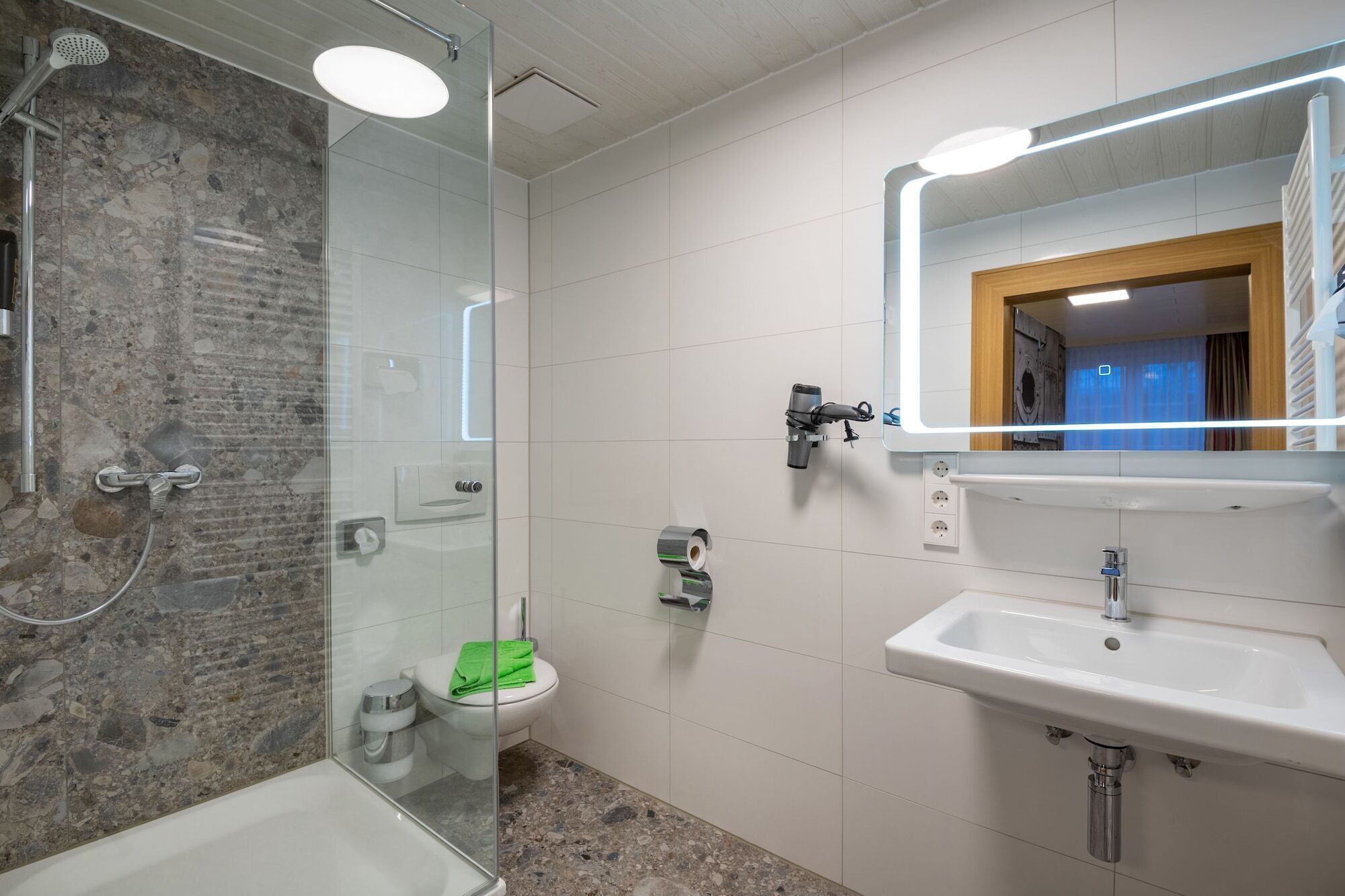 Ein modernes Badezimmer mit einer einachig abgetrennten Dusche, Toilette und Waschbecken mit Spiegel darüber.