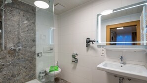 A modern bathroom with a glass-enclosed shower, a toilet, and a sink with a mirror above it. - Seerose (Lindau)