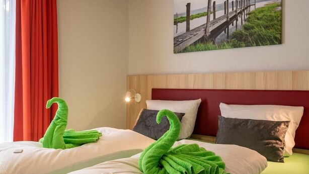 A hotel room with two beds, each with a green towel shaped like a swan. - Seerose (Lindau)