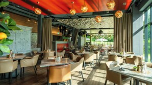 A restaurant with multiple dining tables and chairs, a patterned ceiling, and large windows allowing natural light. - A-ja Bad Saarow. Das Resort (Bad Saarow)