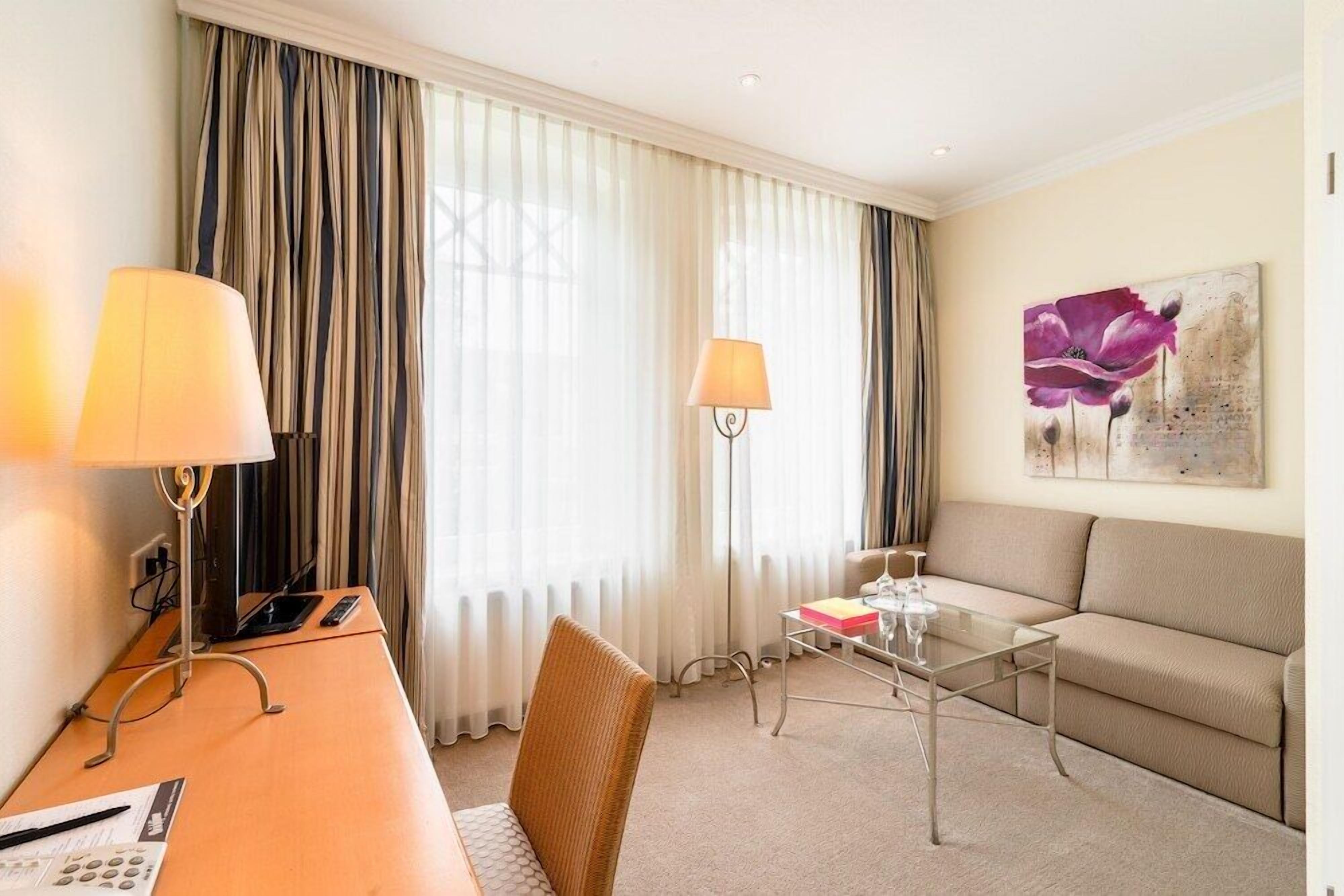 Ein Hotelzimmer mit Schreibtisch, Stuhl, Sofa und Glastisch.