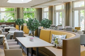 A modern hotel lobby with seating areas, large windows, and indoor plants. - Ringhotel Ostseehotel Ahlbeck (Heringsdorf)