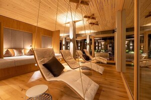 Un área de descanso moderna con suelo y techo de madera, sillones acolchados y un rincón de estar con sofá y cojines.