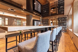A bar area with a long counter, multiple stools, and a wine rack in the background. - Romantik Hotel Sackmann (Baiersbronn)