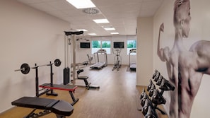 Ein Fitnessraum mit Trainingsgeräten, Laufband und einer Wand mit einer Darstellung einer muskulösen Figur.