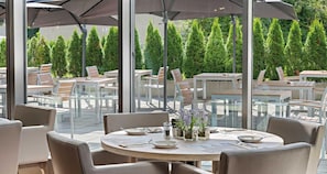 An outdoor dining area with round tables, chairs, and umbrellas. - Hotel Newton Heilbronn (Heilbronn)