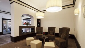 Un hall d’entrée doté d’un espace détente avec des canapés et des poufs, une petite table sur laquelle est posé un vase, et un mur décoratif agrémenté d’une bibliothèque.