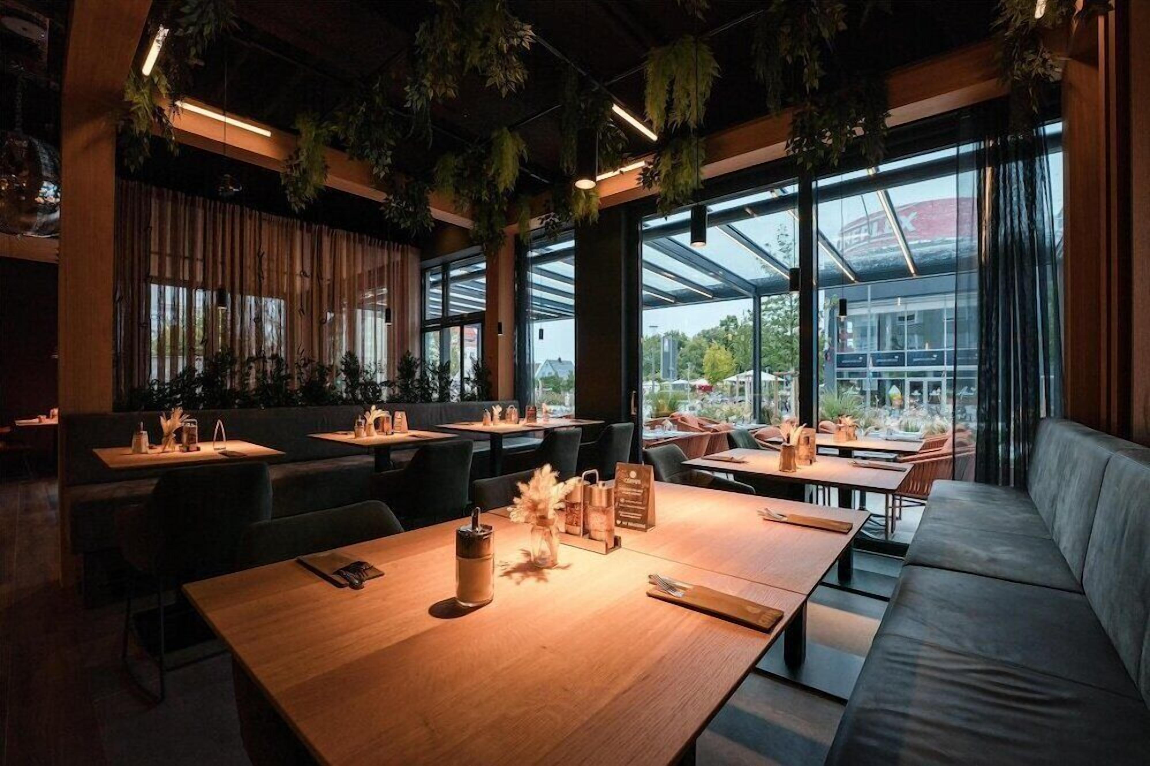 Un interior de restaurante moderno con mesas de madera, sillas negras y un sofá gris.