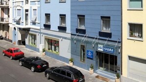 A multi-story hotel with a blue facade, several parked cars, and a visible sign for 'HH HAMM'. - Hamm (Koblenz)